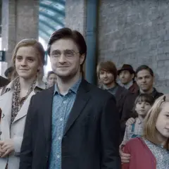 Harry Potter, z charakterystyczną blizną, stoi w tłumie na dworcu. Obok niego Hermiona i Ron.