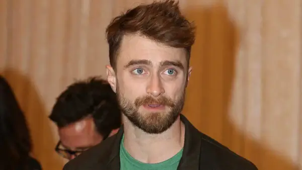 Daniel Radcliffe z zarostem i niebieskimi oczami, jego spojrzenie sugeruje troskę o zdrowie, być może związaną z jego chorobą.